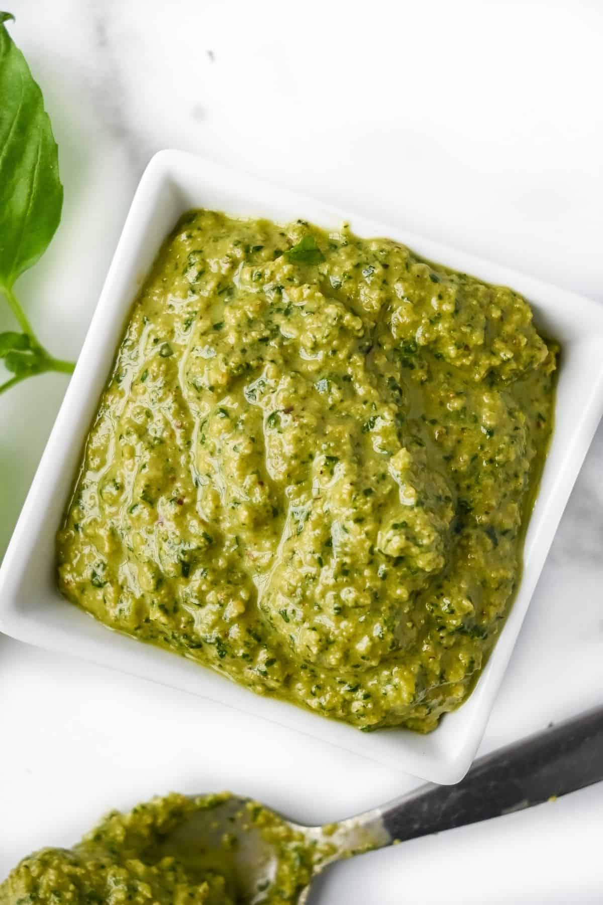 dairy-free pesto in a white square dish with a spoon on a white background.