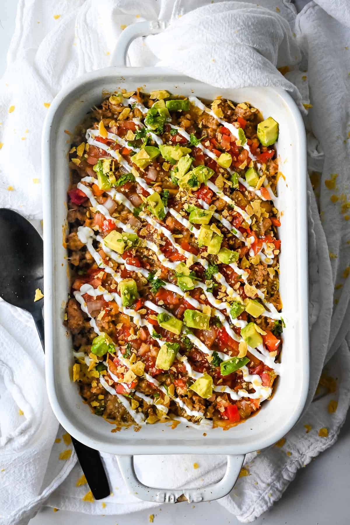 full view of walking taco casserole in a white casserole dish on a white background.
