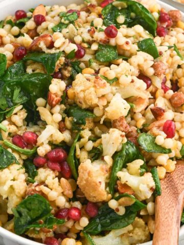 close up of winter roasted cauliflower salad in a white bowl with a wooden spoon.