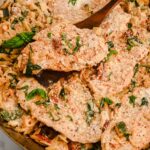 close up of creamy orzo with chicken in a skillet with a wooden spatula, topped with basil.